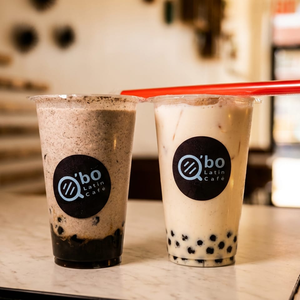 Two Q’bo Latin Café bubble tea drinks with black tapioca pearls and red straws on a café counter.