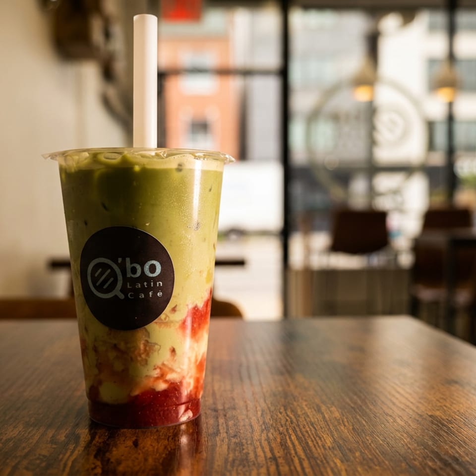 Iced green tea latte with strawberry layers in a branded cup, sitting on a wooden café table.